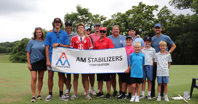 AM Stabilizers's employees and families posing in front of AM Stabilizers sign at the Creekside Classic